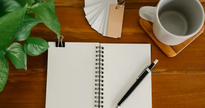 Blank notebook and pen beside a mug and green plant