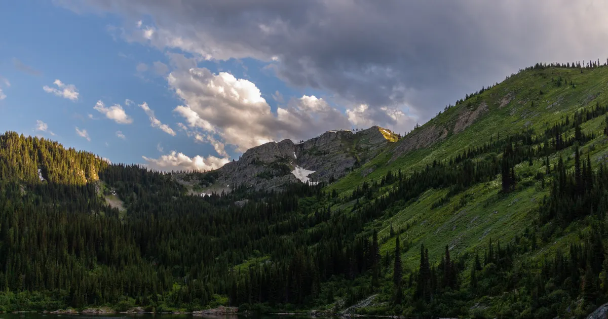 Green mountain slopes and forest beneath a partly cloudy sky
