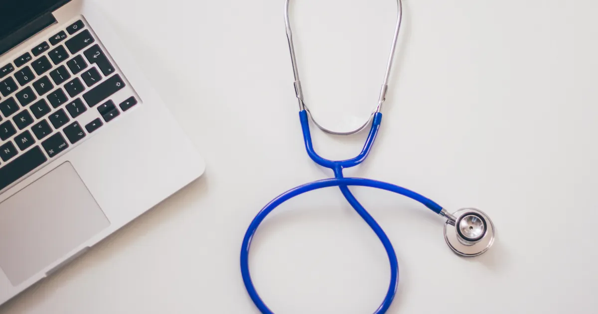 A blue stethoscope beside a laptop on a white desk