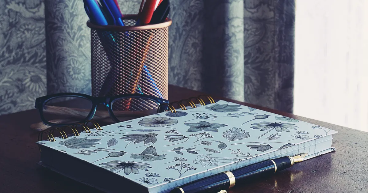 A patterned notebook and a cup of pens on a wooden desk
