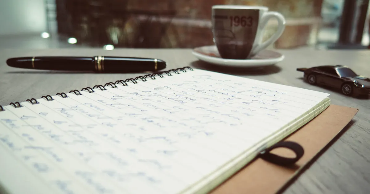 A handwritten notebook and pen beside a coffee cup