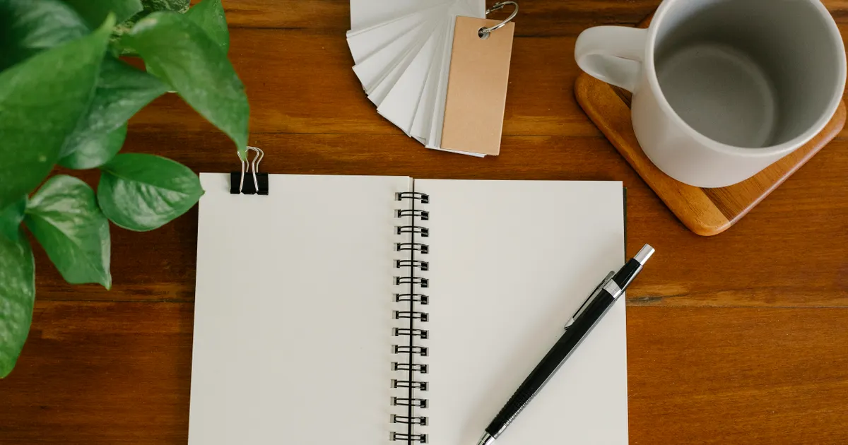 An open blank notebook with a pen beside a potted plant