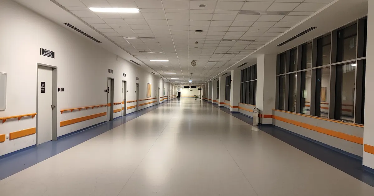 A bright, empty hospital corridor with handrails and open doorways