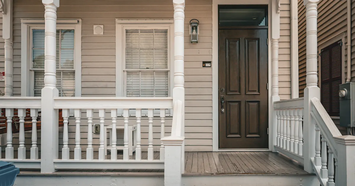 A quiet wooden porch with a front door, columns and white railing