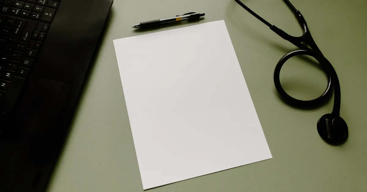 A stethoscope and blank clipboard beside a laptop on a desk
