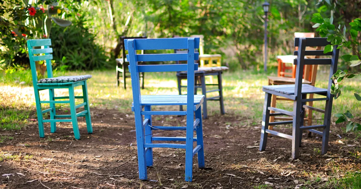 Colorful wooden chairs arranged in a circle in a leafy garden
