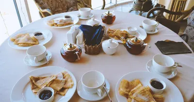 A breakfast table set with teacups, a teapot and plates of crepes