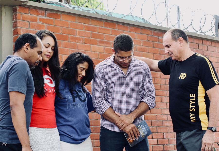 A group of adults praying together, heads bowed in a circle